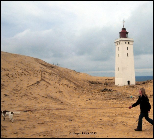 Frau mit Hund vor Leuchtturm auf Sanddüne